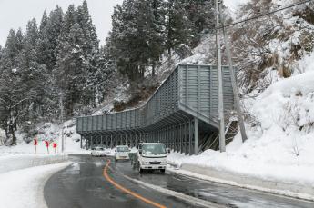 急斜面沿いの道路を走る車を雪崩から守る防護柵の写真