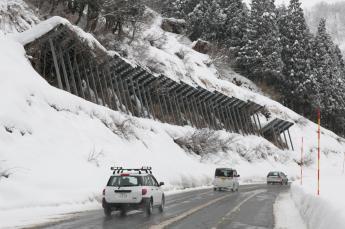 車道の左上に設置されている雪崩予防柵の写真