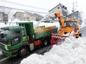 ロータリー除雪車が雪をトラックの荷台に吐き出している様子の写真
