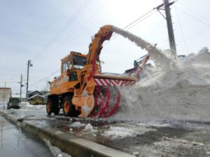 ロータリー除雪車が雪を道路の右側へ吹き出している様子の写真