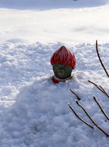 雪に埋もれた赤い頭巾を被ったお地蔵様の写真