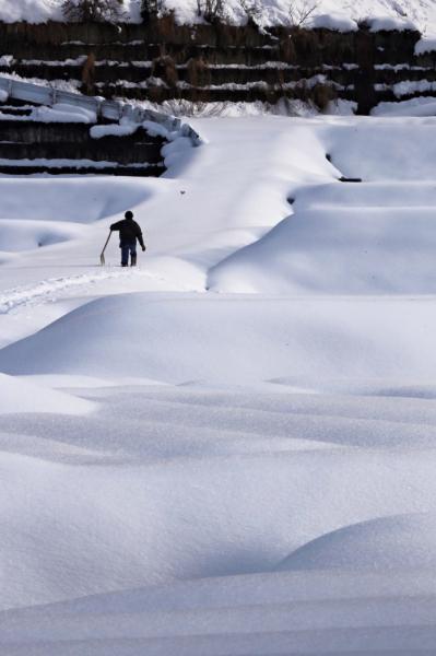 白い雪原の中、遠くでスコップを持って歩く男性の写真