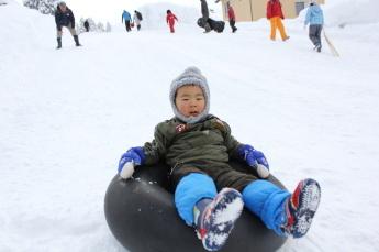 タイヤチューブに座って雪の斜面を降りてきている少年の様子の写真