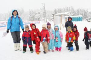 雪の中でも目立つ様にカラフルなスキーウェアを纏って登下校する子供たちと保護者の写真