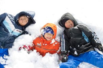 雪に寝っ転がって笑っている3人の男の子の様子の写真