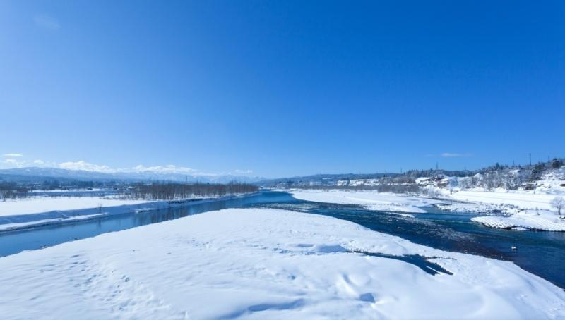 雪が積もって一面の雪景色の中で流れる川の風景写真