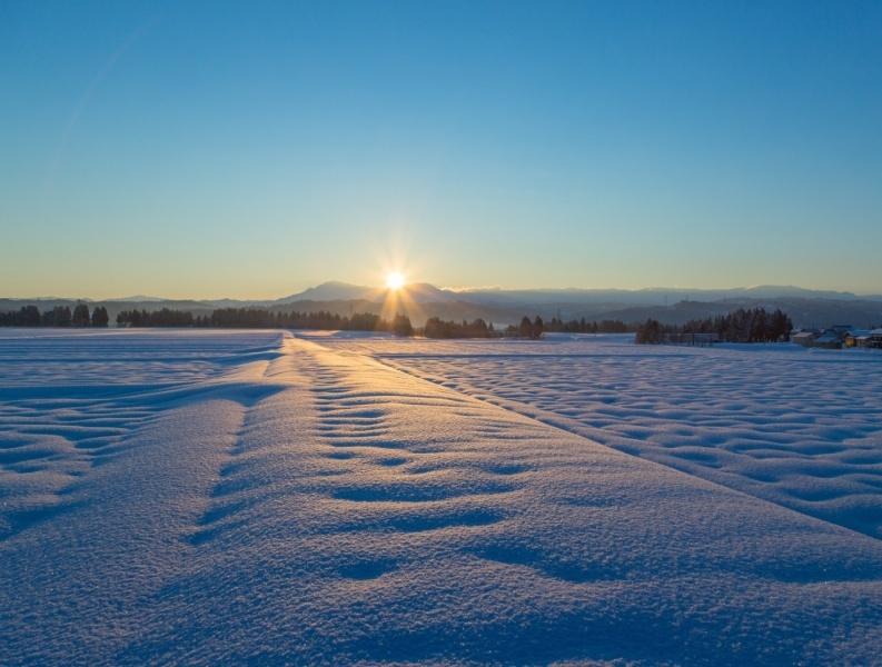 夕日が沈みオレンジ色の光が雪に映し出されている風景写真