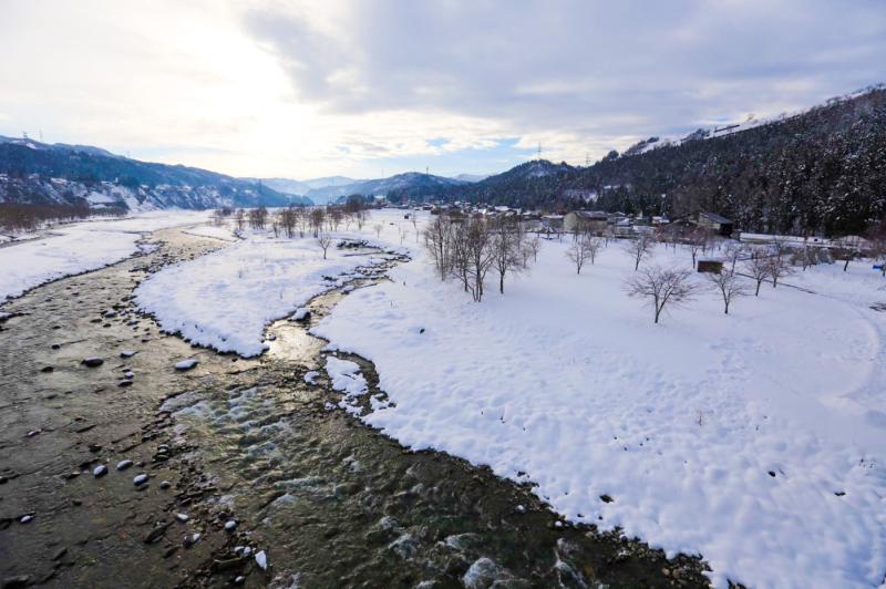 雪が積もる町の横を流れる川の風景写真