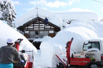 大人の身長以上に積もった雪を男性たちが、雪下ろししている処の写真