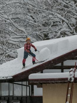 屋根に1メートルほど積もった雪を除雪している様子の写真