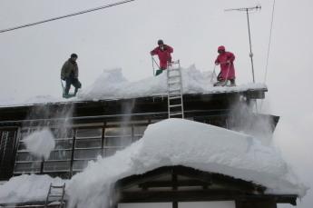 3人がかりで屋根に積もった雪を除雪しようとしている様子の写真