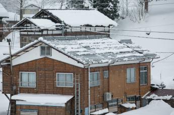 屋根の雪のほとんどが熱で溶け落ちている融雪式住宅の様子の写真