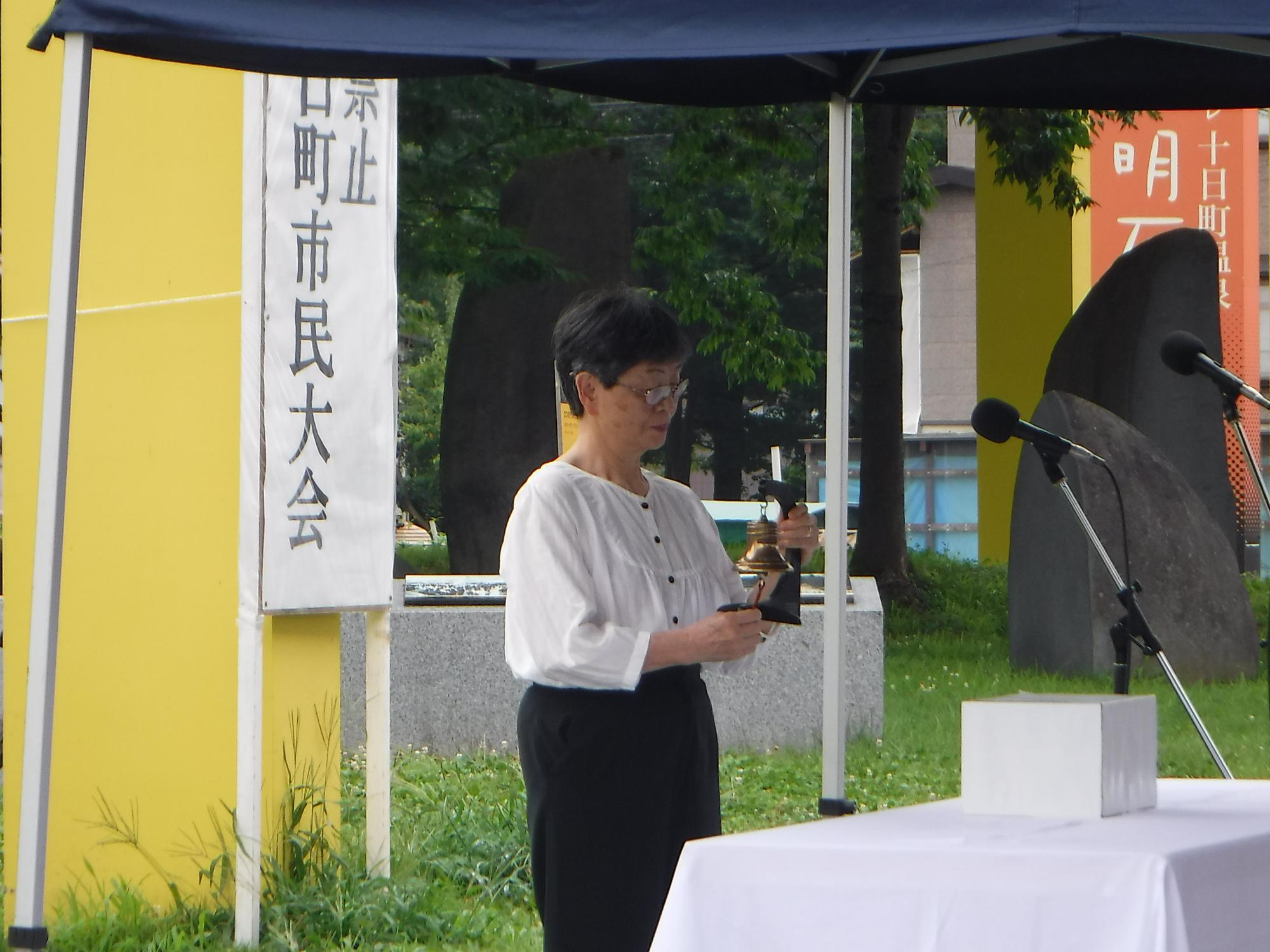 十日町市民大会で、会長がアンジェラスの鐘を鳴らすのに合わせて黙とうをする様子