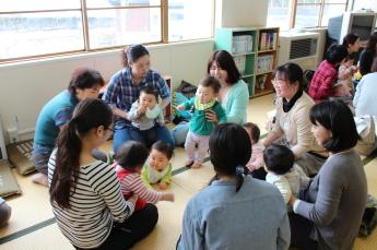 十日町市中央公民館の一室で両手で乳児を支えながら輪になって楽しそうに子育ての話をする母親たちの写真