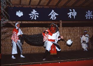 白い衣装に黒い布と赤いお面をつけた獅子舞が舞台上でパフォーマンスしている写真