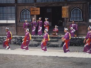 紫の着物の女性が建物の前で踊っている写真