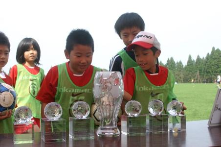 子どもたちが机に並んだクリスタルのカップを眺めている写真