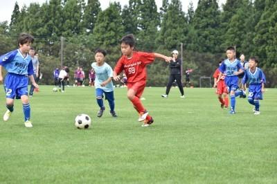 赤いユニフォームの児童と青いユニフォームの児童がボールを追いかけあっている写真