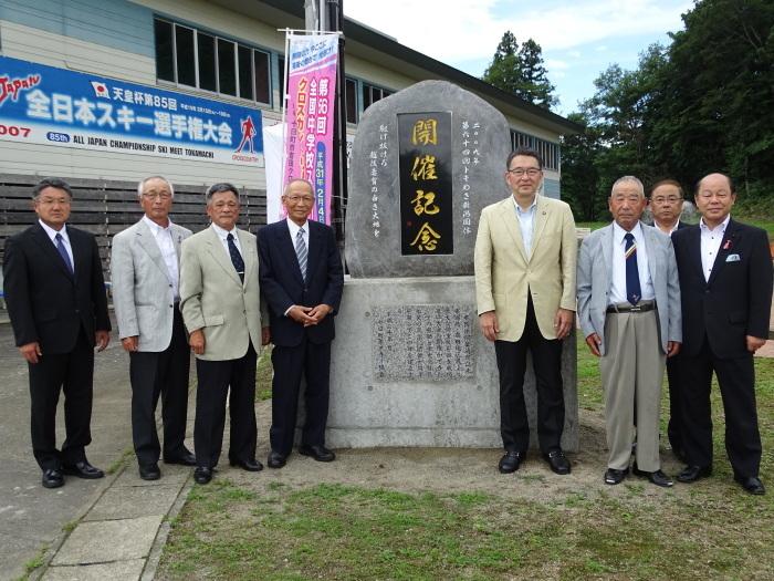 開催記念の石碑の周りに並んで立って記念撮影をする男性たちの写真