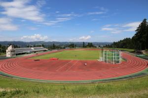 青い空と白い雲、芝生と徒競走レーンがある十日町市陸上競技場の写真