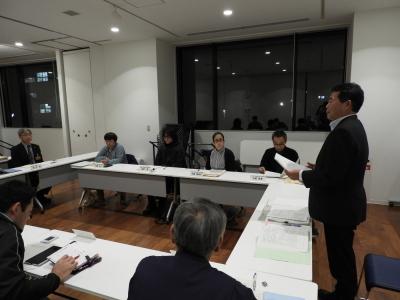 大きな窓のある会議室内で委員会が行われている写真