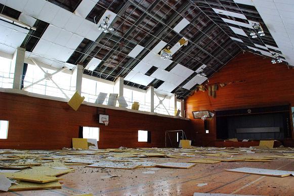 地震で体育館内部の屋根のパネルが落ちて床に散乱している写真