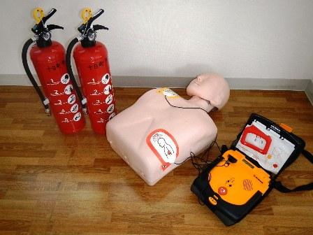 床の上に水消火器と模擬AED・マネキン人形セットが置かれている写真