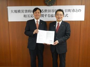 2人の背広の男性が災害時応援協定の調印書を2人で持って微笑んでいる写真